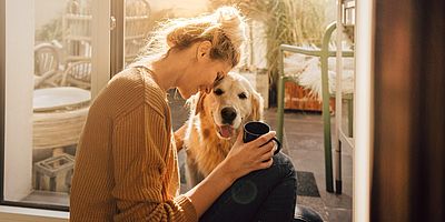 Glückliche Frau mit Hund in ihrer Wohnung mit Kaffeetasse in der Hand